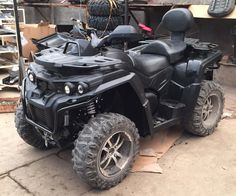 a black four - wheeler parked in a garage next to some tires and other items