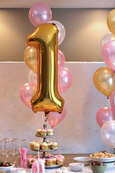 a birthday party with balloons, cake and cupcakes in the shape of a number one