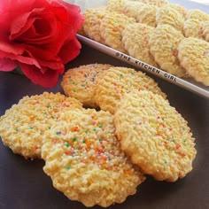 three cookies with sprinkles are next to a red rose on a table