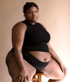 a woman sitting on top of a wooden stool wearing a black dress and high heels