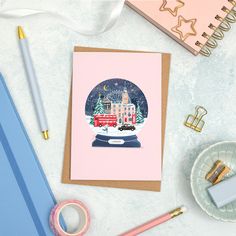 a card with a snow globe in the center surrounded by stationery and office supplies