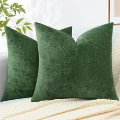 two green pillows sitting on top of a white couch next to a potted plant