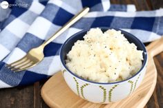 a bowl filled with mashed potatoes on top of a wooden cutting board next to a fork