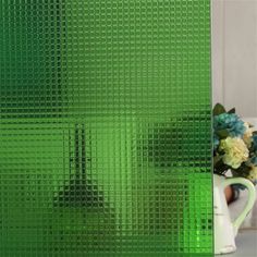 a vase filled with flowers sitting next to a green glass window covering that has squares on it