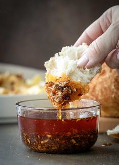 a person dipping something into a bowl with some sauce on it and bread in the background