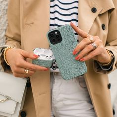 a woman holding a cell phone in her hand and wearing a trench coat with white pants