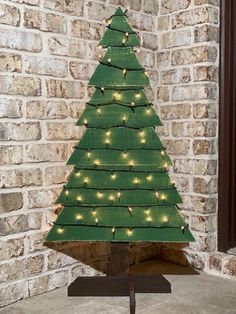 a small green christmas tree with lights on it in front of a brick wall and window