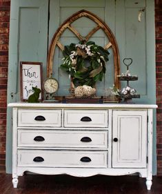 an old dresser with flowers and plants on top is in front of a blue wall