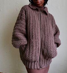 a woman standing in front of a white wall wearing a purple sweater and pink skirt