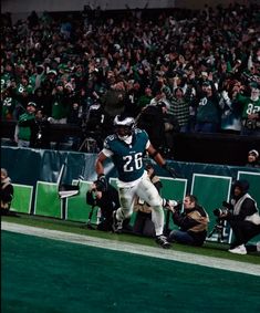 a football player running on the field with fans in the stands watching from the sidelines