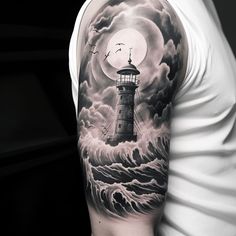 a man's arm with a lighthouse tattoo on it and clouds in the background