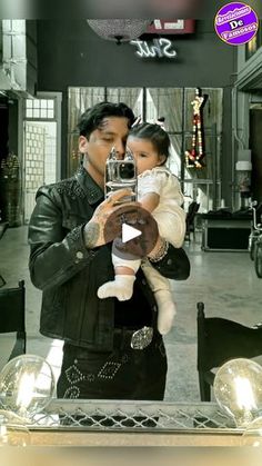 a man holding a baby taking a selfie in front of a mirror with lights