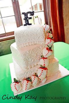 a three tiered cake decorated with baseballs and strawberries sits on a green table