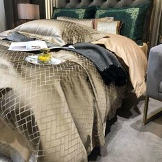 a bed with gold sheets and pillows on top of it next to a gray chair