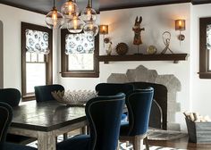 a dining room table with blue chairs in front of a fire place and window sill