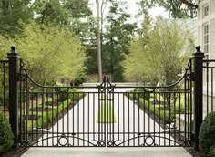 an iron gate in front of a house with trees and bushes around it, leading into the yard