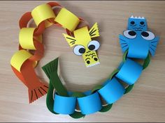 two fish made out of construction paper sitting on top of a wooden table next to an orange and blue ribbon