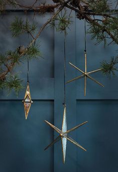 three ornaments hanging from a tree branch in front of a blue door with pine branches