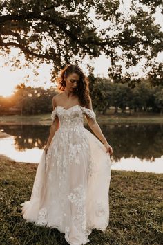 a woman in a wedding dress is standing by the water at sunset with her hands on her hips