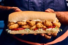 a person holding a sub sandwich with tater tots on it