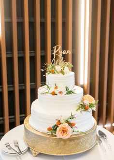 a white wedding cake with flowers and the word love spelled on top is sitting on a gold platter