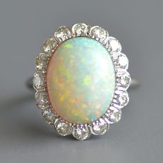 an opalite and diamond ring on a gray surface with the center stone surrounded by small diamonds