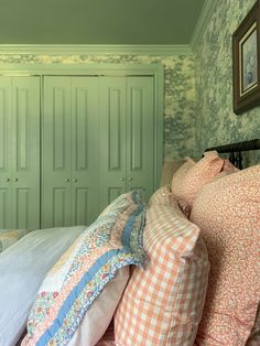 a bed with many pillows on top of it in front of green closets and wallpaper