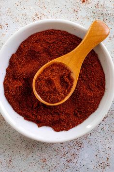 a wooden spoon in a white bowl filled with red powder and ground cinnamon flakes