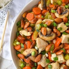 a white bowl filled with carrots, cashews and other vegetables next to chopsticks