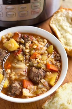 a bowl of beef and barley soup next to an instant pressure cooker with two slices of bread