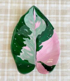 a green and pink leaf shaped dish sitting on top of a checkered table cloth