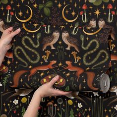 two hands are holding onto a wallpaper with cats and mushrooms on it, while another hand is reaching for the fabric