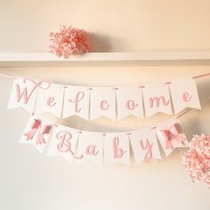 pink and white welcome baby banner hanging from the side of a wall next to flowers