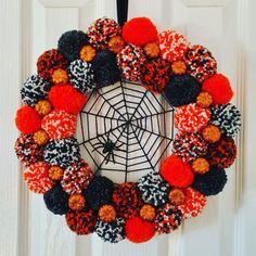 a halloween wreath with pom poms hanging on the front door and spider web