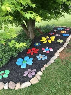 a garden path made out of rocks and stones with colorful flowers on the ground next to a tree