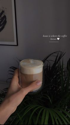 someone holding up a cup of coffee in front of a potted plant with a quote on it