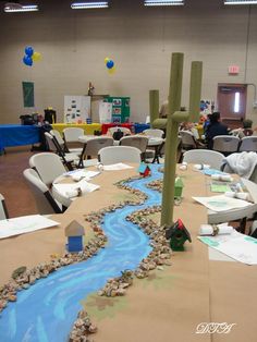 a long table covered in paper and rocks with a river running through the center surrounded by chairs