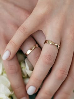 two hands holding each other with wedding rings on their fingers and white flowers in the background