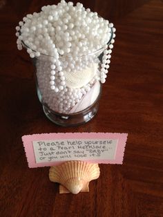 a glass vase filled with white pearls next to a seashell