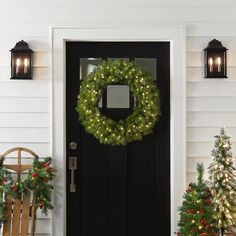 a christmas wreath on the front door of a house with two chairs and trees outside