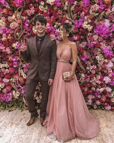 two people standing next to each other in front of a flower wall with pink flowers