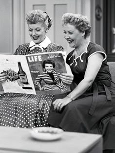 two women are sitting on a couch and one is reading a magazine to another woman