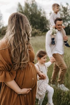 a pregnant woman in a brown dress is holding her baby while two other people are standing behind her