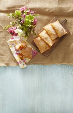 some food is laying out on a table next to a vase with flowers and a cutting board