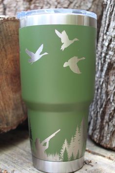 a green tumbler with white birds flying over the trees on it's side