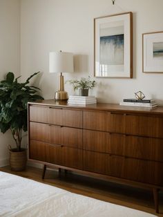 a wooden dresser sitting next to a bed with two pictures on the wall above it