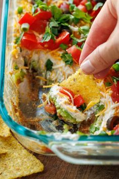 someone is dipping tortilla into a casserole dish with tomatoes, green onions and cheese