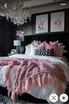 a bedroom with black walls and white bedding, chandelier and pink throw pillows