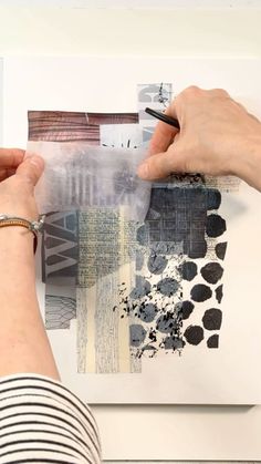 two hands are holding a piece of paper over an art work with black and white designs on it