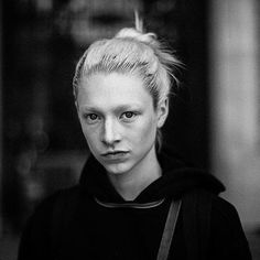 a black and white photo of a woman with blonde hair wearing a hoodie looking at the camera